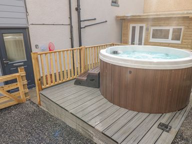 A hot tub on a wooden deck with a black door and wooden fence in the background at Coeden Bach in Burry Port