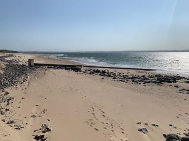 A sandy beach with rocks and a concrete structure by the sea at Coeden Bach in Burry Port