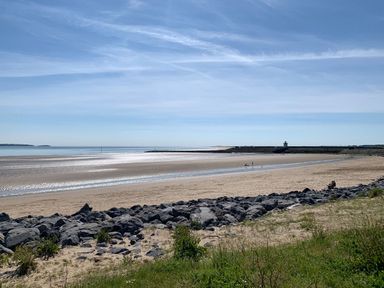 A sandy beach with rocks in the foreground and a body of water with a lighthouse in the distance at Coeden Bach in Burry Port