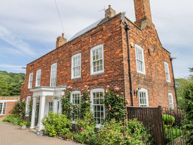A brick house with white windows and columns with flowers and plants around at The Manor House in Scarborough