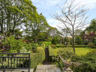A garden with trimmed hedges a stone path a basketball hoop and trees at The Manor House in Scarborough
