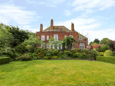 A garden with trimmed hedges trees and a lawn in front of a brick house at The Manor House in Scarborough