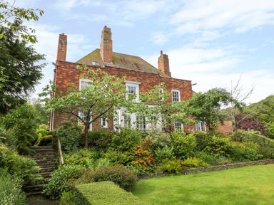 A red brick house with multiple chimneys surrounded by a garden with trees shrubs and lawn at The Manor House in Scarborough