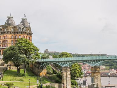 A historic building with conical roofs next to a green iron bridge over a river at The Manor House in Scarborough