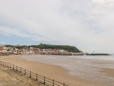 A beach with wet sand and a town with buildings and green hills in the background at The Manor House in Scarborough