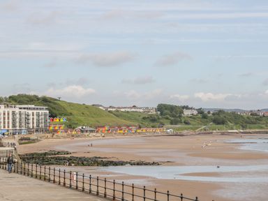 A beach with colorful beach huts along the shore and buildings on a hill at The Manor House in Scarborough