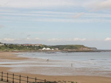 A beach with wet sand and tide pools with a few people walking near water with houses and grassy hills in the background at The Manor House in Scarborough