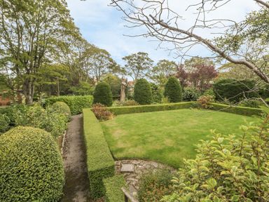 A garden with trimmed hedges trees and a grass lawn at The Manor House in Scarborough