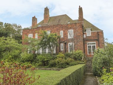 A brick house with multiple chimneys and white windows surrounded by trees and shrubs at The Manor House in Scarborough