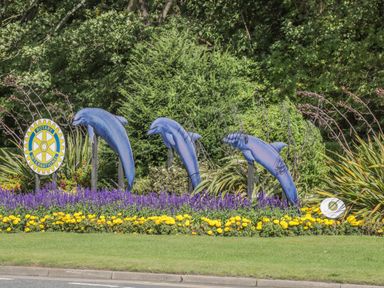 A garden display with three blue dolphin sculptures and colorful flowers at The Manor House in Scarborough
