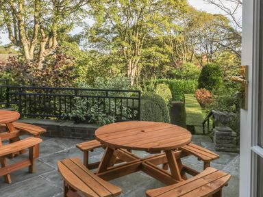 A patio with wooden round picnic tables overlooking a garden with trees and bushes at The Manor House in Scarborough