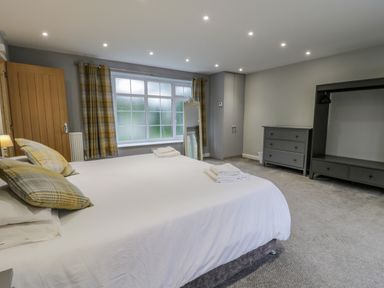 A bedroom with a bed pillows dresser open wardrobe and a window with curtains at The Manor House in Scarborough