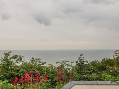 A view of the sea with green and red flowering plants in the foreground and a building on the far right at Sea-Prize View in Old Colwyn
