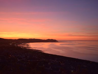 A coastal town at sunset with hills in the background and calm sea at Sea-Prize View in Old Colwyn