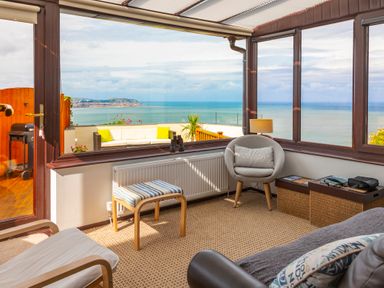 A sunroom with chairs and a footstool overlooking a balcony with a sea view at Sea-Prize View in Old Colwyn