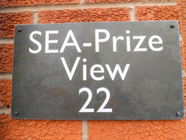 A black sign with white text reading SEA-Prize View 22 mounted on a red brick wall at Sea-Prize View in Old Colwyn