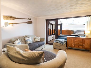 A living room with beige sofas paddles on the wall and a wooden cabinet at Sea-Prize View in Old Colwyn
