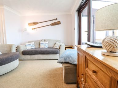A living room with two sofas a wooden sideboard and two paddles on the wall at Sea-Prize View in Old Colwyn
