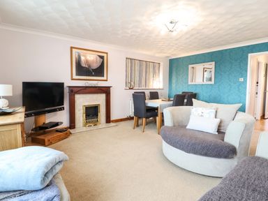A living room with a fireplace dining table chairs and curved sofa at Sea-Prize View in Old Colwyn