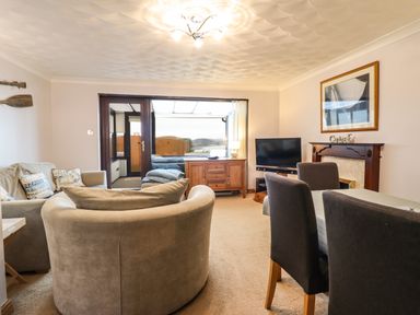 A living room with sofas chairs a dining table a TV and a wooden sideboard at Sea-Prize View in Old Colwyn