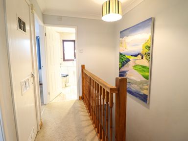 A hallway with wooden railing a colorful painting on the wall and open door leading to a bathroom at Sea-Prize View in Old Colwyn