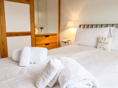 A bedroom with a bed with white sheets and pillows a lamp on a nightstand and rolled white towels on the bed at Sea-Prize View in Old Colwyn
