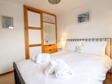 A bedroom with a bed with white linens and towels on it a nightstand with a lamp and decorated wall at Sea-Prize View in Old Colwyn