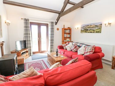 A living room with red sofas a wooden coffee table a television and French doors at Dale View Cottage in Allendale near Hexham