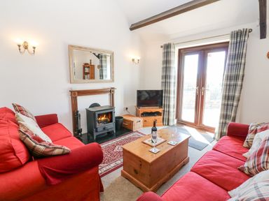 A living room with two red sofas a wooden coffee table a wood burning stove and glass doors with plaid curtains at Dale View Cottage in Allendale near Hexham