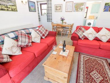 A living room with two red sofas wooden coffee table and a dining table at Dale View Cottage in Allendale near Hexham
