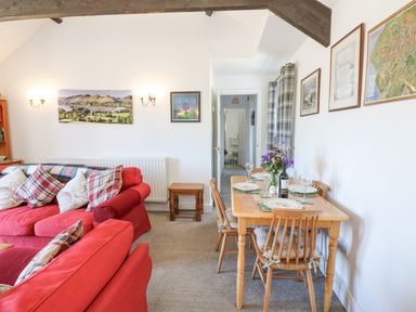 A living room with red sofas and a dining table set with plates and glasses at Dale View Cottage in Allendale near Hexham