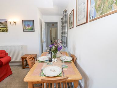 A dining table set with plates glasses and flowers in a room with wall art and a red sofa at Dale View Cottage Allendale near Hexham
