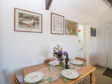 A dining table set for four with plates glasses and a bottle of wine with framed pictures on the wall at Dale View Cottage in Allendale near Hexham
