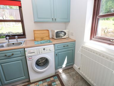A kitchen corner with a washing machine, microwave, wooden bread box, sink, and blue cabinets at Dale View Cottage in Allendale near Hexham
