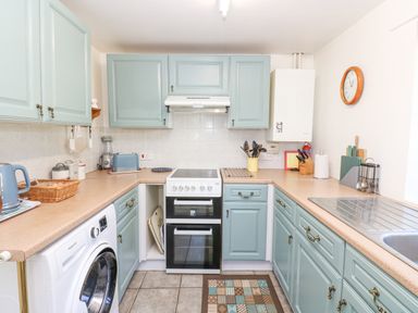 A kitchen with blue cabinets a stove a washing machine and a sink at Dale View Cottage in Allendale near Hexham