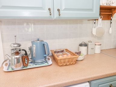 A kitchen countertop with a kettle and teapot on a tray eggs in a basket containers labeled coffee tea sugar and a small bowl of grapes at Dale View Cottage Allendale near Hexham