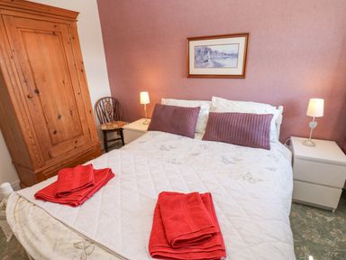 A bedroom with a double bed two red towels on it two bedside tables with lamps a wooden wardrobe and a wooden chair at Dale View Cottage in Allendale near Hexham