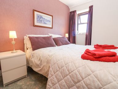 A bedroom with a bed with pillows and folded towels bedside tables with lamps and a window with curtains at Dale View Cottage in Allendale near Hexham