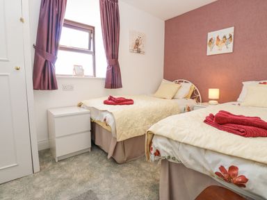 A bedroom with two single beds a bedside table with a lamp and purple curtains at Dale View Cottage in Allendale near Hexham
