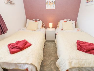 A bedroom with two single beds separated by a white nightstand and a lamp at Dale View Cottage in Allendale near Hexham