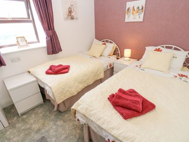 A bedroom with two single beds bedside tables and red towels at Dale View Cottage in Allendale near Hexham