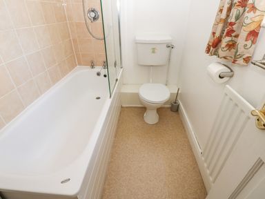 A bathroom with a bathtub a toilet a toilet brush a radiator and a window with floral curtains at Dale View Cottage in Allendale near Hexham