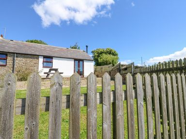 A view of a stone and white cottage with a wooden picket fence and green lawn at Dale View Cottage in Allendale near Hexham