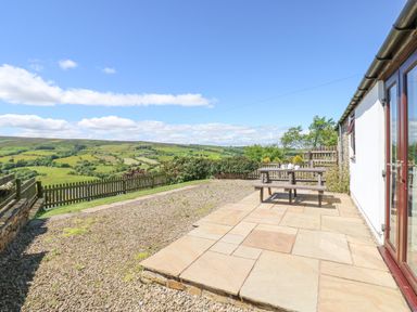 A patio with a wooden picnic table outside a white building overlooking a fenced countryside view at Dale View Cottage in Allendale near Hexham