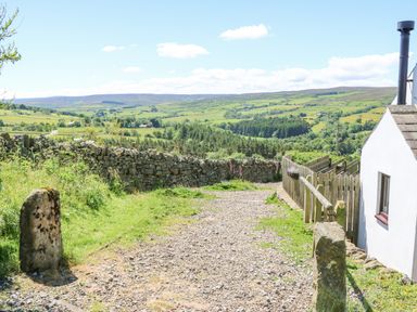 A gravel path with stone walls and a white building overlooking green fields and hills at Dale View Cottage in Allendale near Hexham