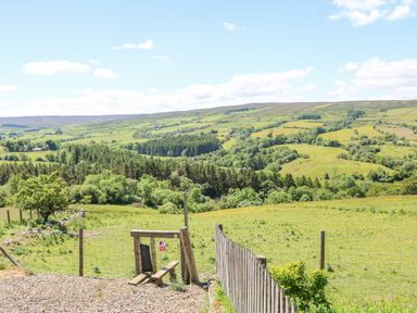 A rural landscape with green fields trees and hills viewed over a wooden fence and gate at Dale View Cottage in Allendale near Hexham