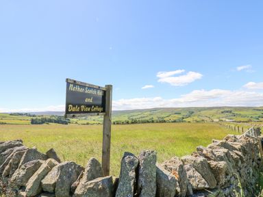 A sign on a wooden post behind a stone wall overlooking a green field with hills in the background at Dale View Cottage in Allendale near Hexham