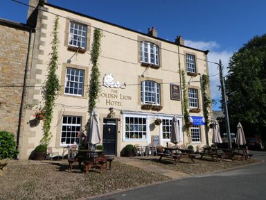 The exterior of The Golden Lion Hotel with outdoor seating and umbrellas at Dale View Cottage in Allendale near Hexham