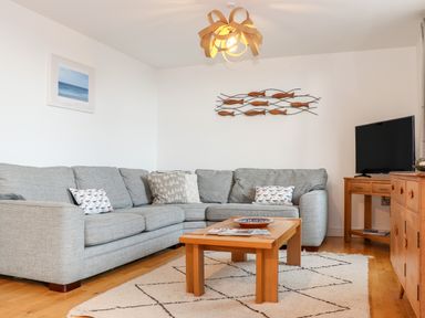 A living room with a gray sectional sofa wooden coffee table and television at Ocean Blue in Praa Sands