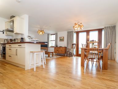 An open plan kitchen and dining area with wooden floor and chairs at Ocean Blue in Praa Sands